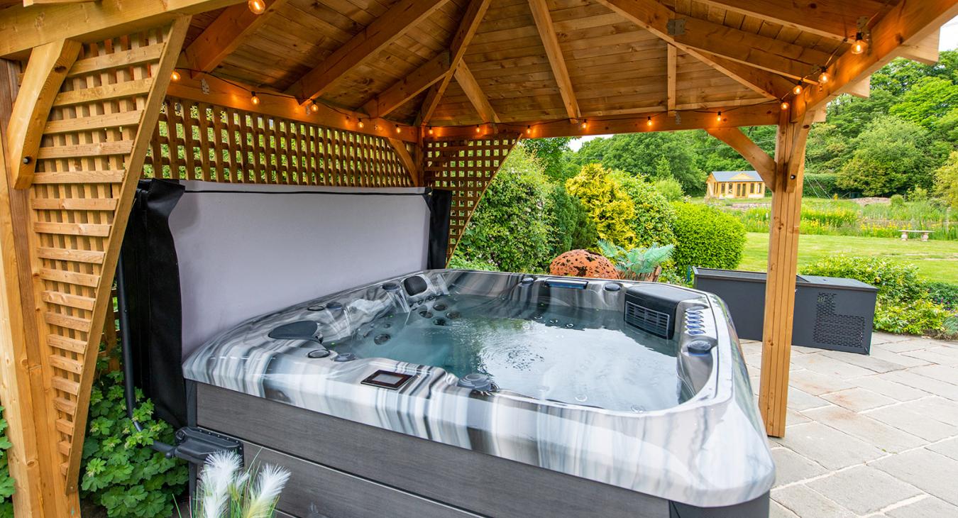 Outdoor hot tub installed under a wooden gazebo, creating a private backyard spa setting.