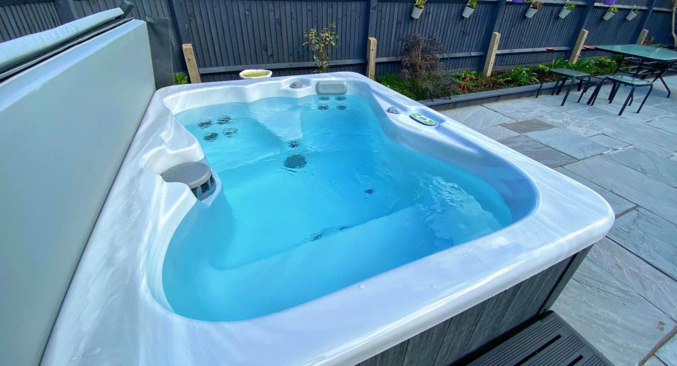 Compact backyard hot tub with clear water, steps, and surrounding garden landscaping.
