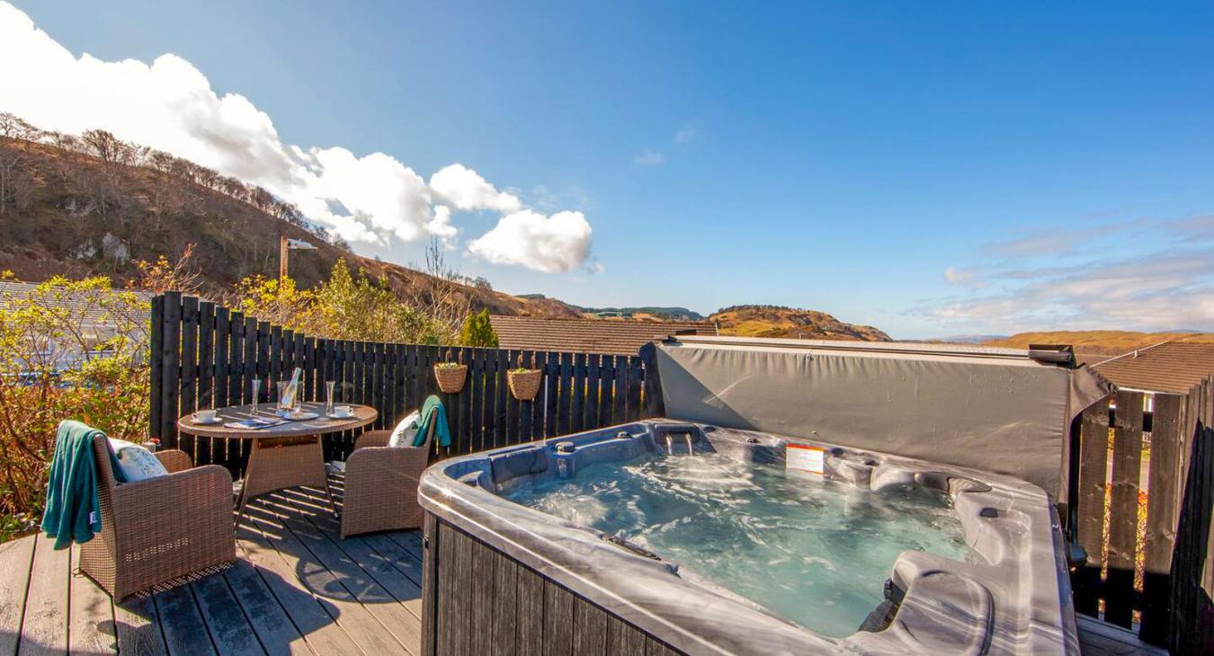 Hot tub installed on a wooden deck with outdoor furniture and mountain views in the background.